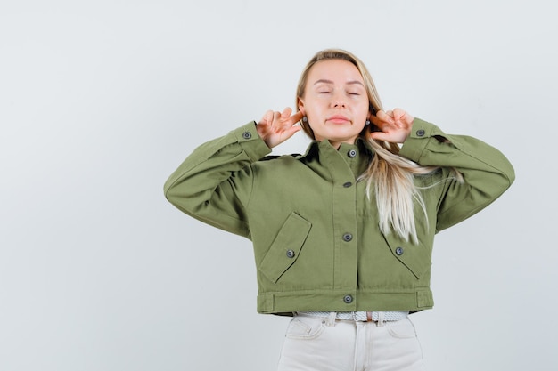 Free photo blonde lady plugging ears with fingers in jacket, pants and looking relaxed. front view.