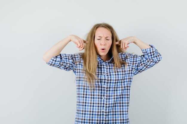 Blonde lady plugging ears with fingers in shirt and looking annoyed ,