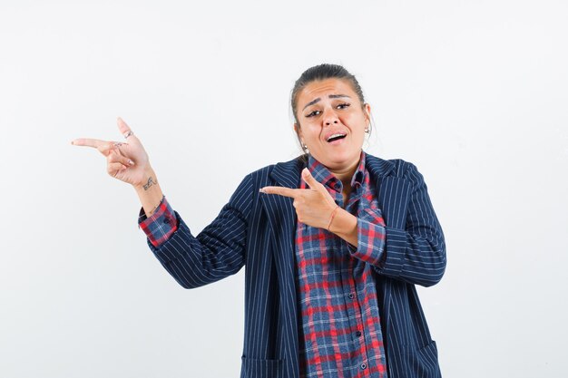 Blonde lady pointing aside in shirt, jacket and looking helpless. front view.