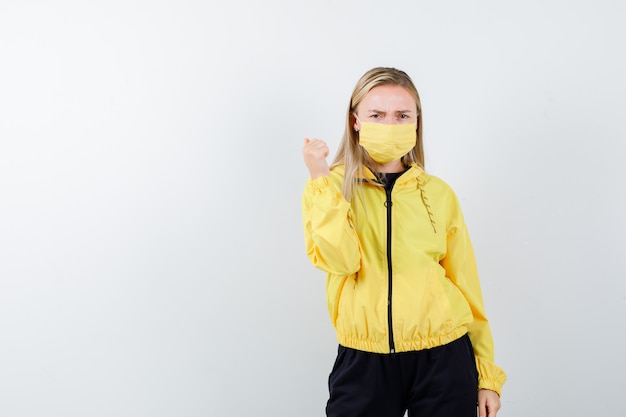 Free Photo blonde lady pointing back with thumb in tracksuit, mask and looking offended , front view.