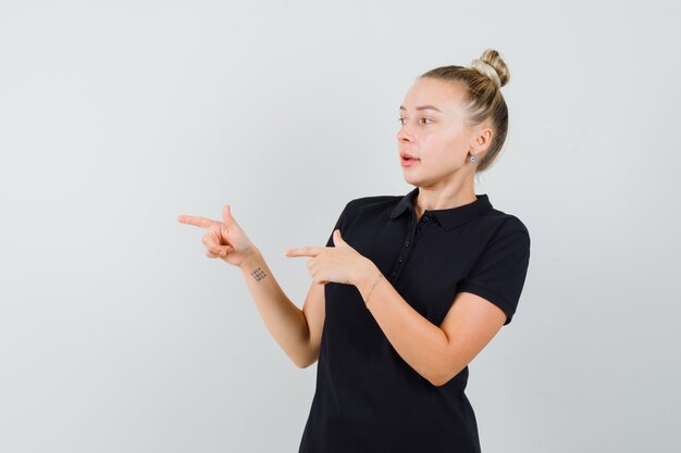 Blonde lady pointing to the side in black t-shirt and looking focused. front view.