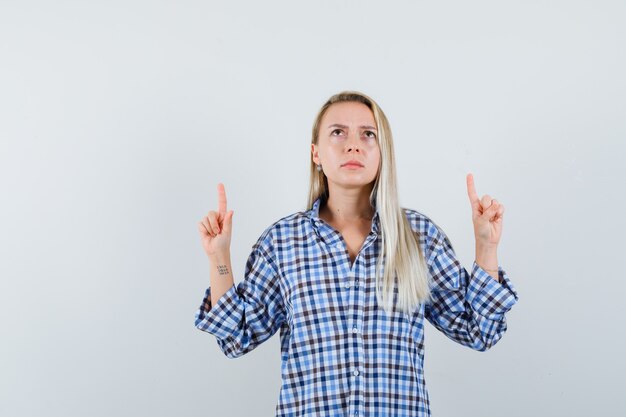 Blonde lady pointing up in checked shirt and looking serious