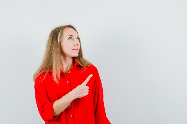 Blonde lady pointing up in red shirt and looking hopeful ,