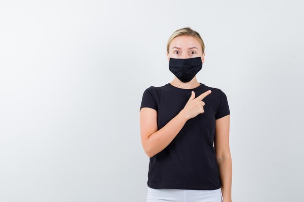 Blonde lady pointing at upper right corner in black t-shirt isolated