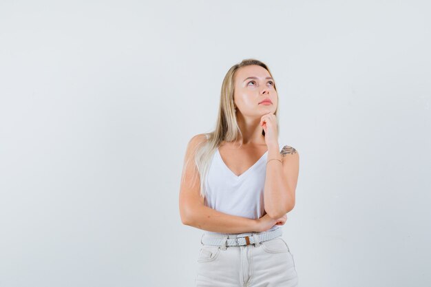 Blonde lady propping chin on hand in singlet, pants and looking pensive