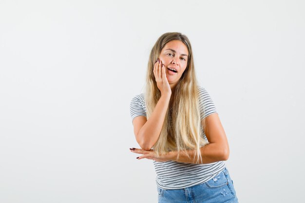 Blonde lady putting hand her face in t-shirt and looking confident. front view.