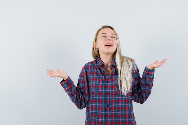 Blonde lady raising open palms in casual shirt and looking grateful. front view.