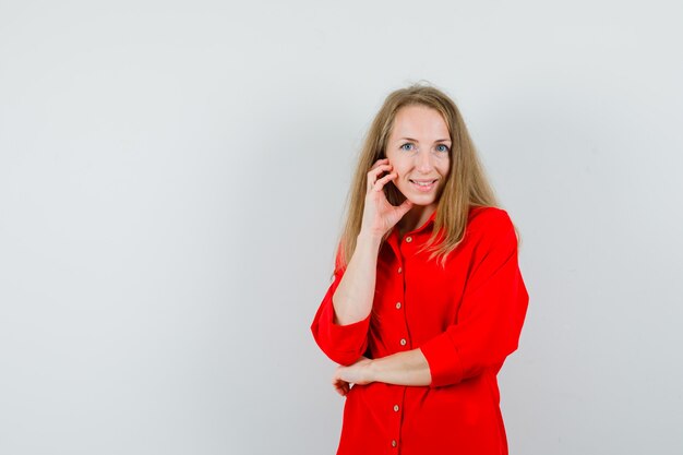 Blonde lady in red shirt holding hand on cheek and looking merry ,