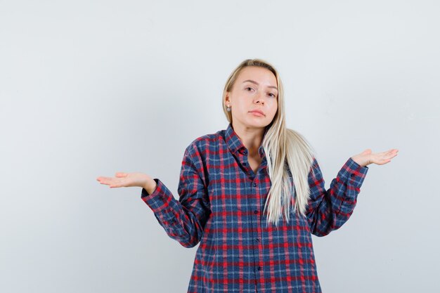 Blonde lady showing helpless gesture in casual shirt and looking confused. front view.