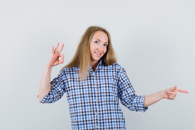 Blonde lady showing ok sign, pointing aside in shirt and looking frisky.