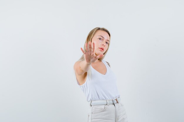 Blonde lady showing refusal gesture in singlet, pants and looking confident