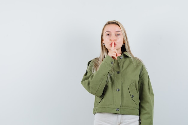 Free Photo blonde lady showing silence gesture in jacket, pants and looking careful , front view.