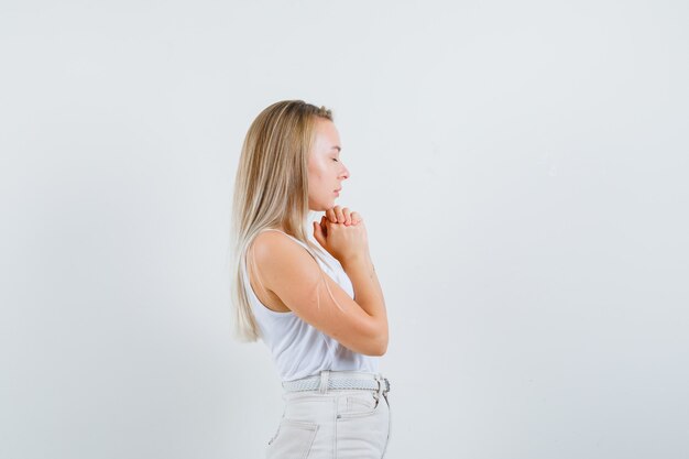 Blonde lady in singlet, pants clasping hands in praying gesture and looking hopeful .