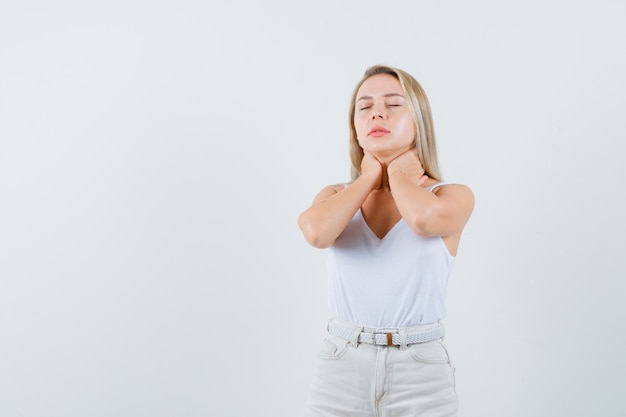 Blonde lady in singlet, pants holding hands on neck and looking fatigued