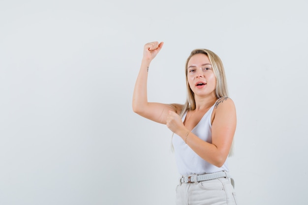 Blonde lady in singlet, pants showing winner gesture and looking happy