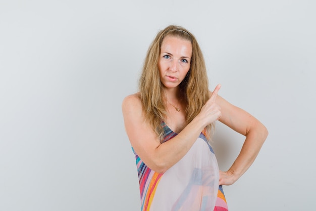 Blonde lady in summer dress pointing up and looking confident 