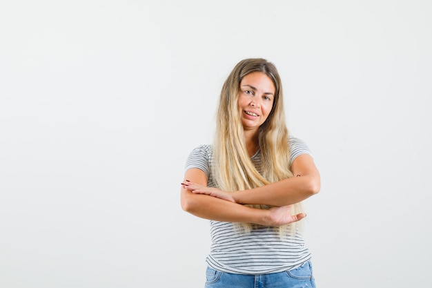 Blonde lady in t-shirt crossing her arms while smiling and looking coy , front view.