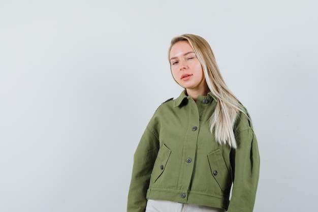 Blonde lady winking eye in jacket, pants and looking confident , front view.