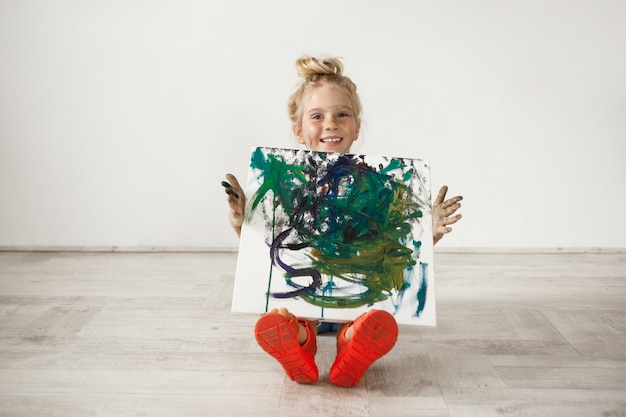 blonde little girl with freckled face and hair bun showing picture to her parents.