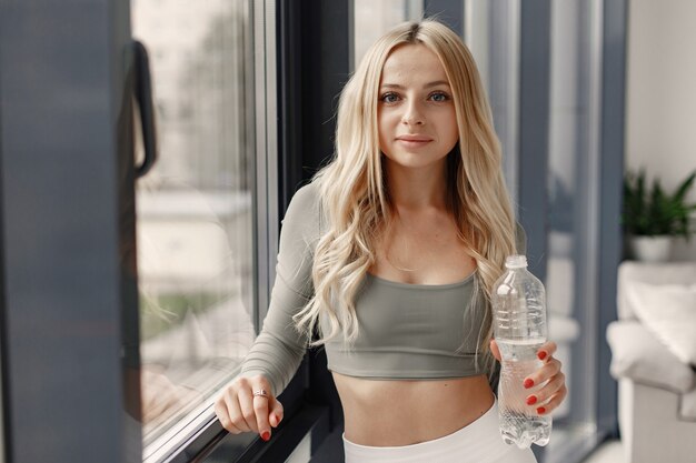 Blonde posing. Lady in a sport suit. Woman at home by the window.