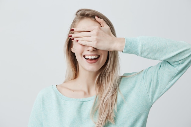 Blonde pretty woman closing her eyes with hand, having happy expression, smiling broadly