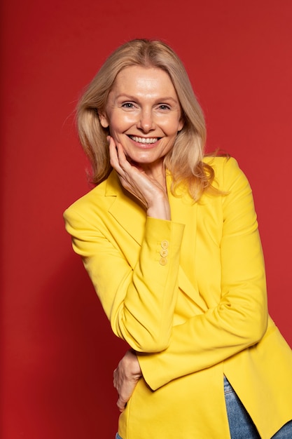 Blonde senior woman posing and smiling against a red background