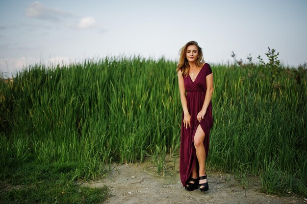 Blonde sensual woman in red marsala dress posing in the reeds