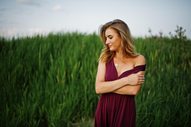 Blonde sensual woman in red marsala dress posing in the reeds