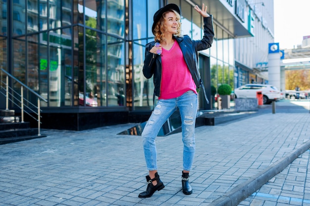 blonde short haired woman walking on streets of big modern city. Fashionable urban outfit. Unusual pink sunglasses.