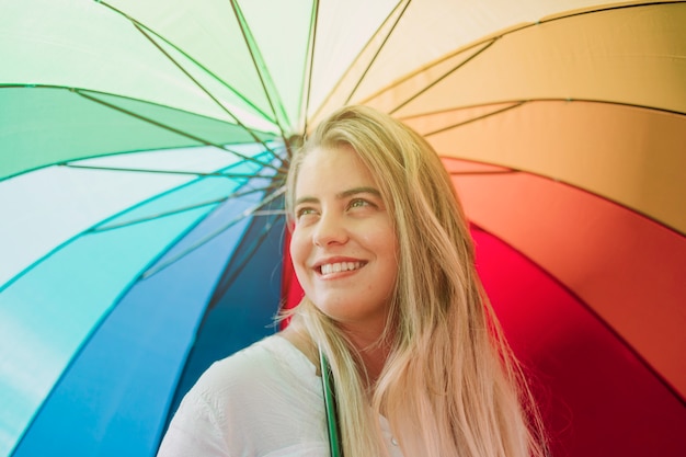 Free photo blonde smiling young woman holding rainbow umbrella