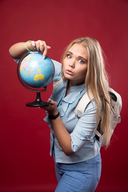 Free Photo blonde student woman holds a globe and looks surprized.