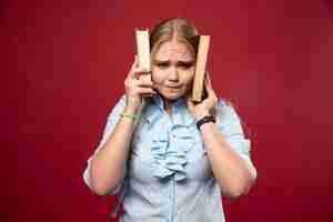 Free photo blonde student woman holds her books and covers her ears with them.