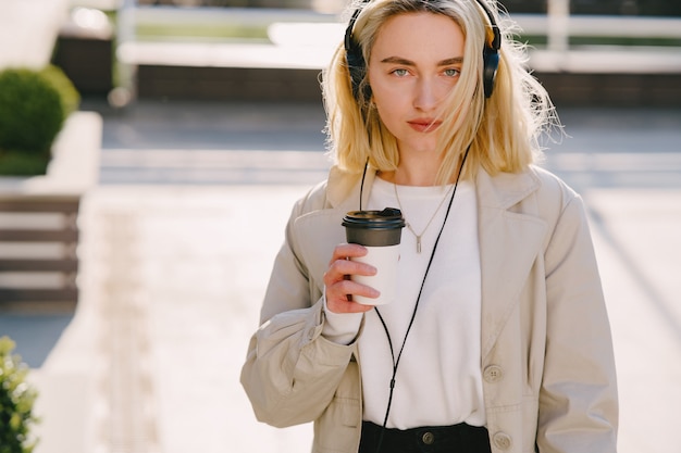 Blonde walks in summer city with cup of coffee