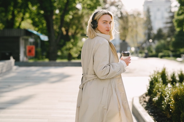 Blonde walks in summer city with cup of coffee