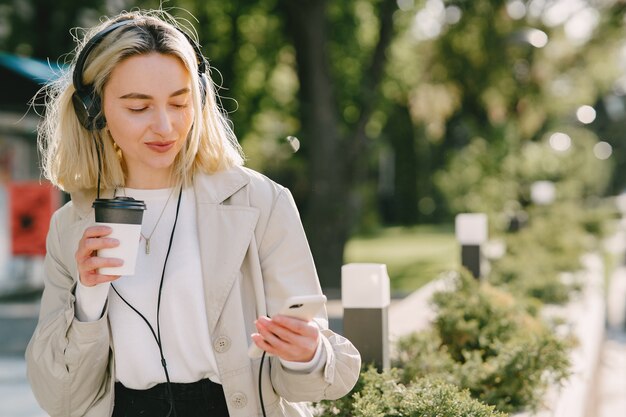 Free photo blonde walks in summer city with cup of coffee