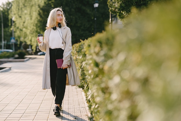 Free photo blonde walks in summer city with cup of coffee