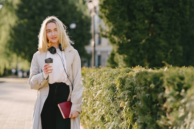 Blonde walks in summer city with cup of coffee