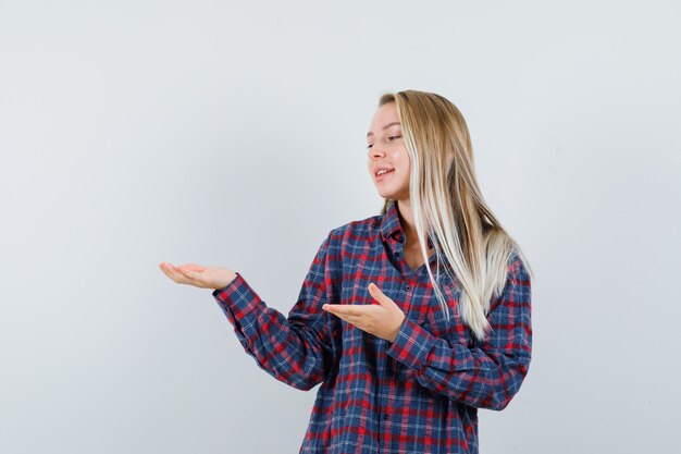 Blonde woman in checked shirt holding hands as holding something and looking at it and looking happy , front view.