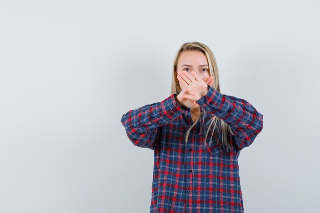 Blonde woman in checked shirt holding hands crossed and looking serious , front view.