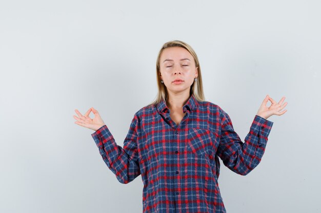 Blonde woman in checked shirt meditating and looking relaxed , front view.