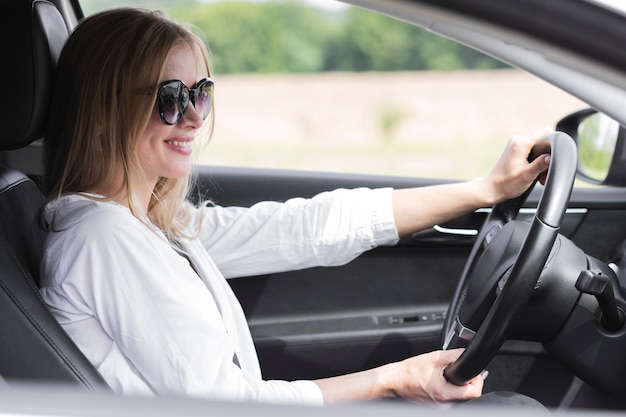 Blonde woman driving a car while wearing glasses 