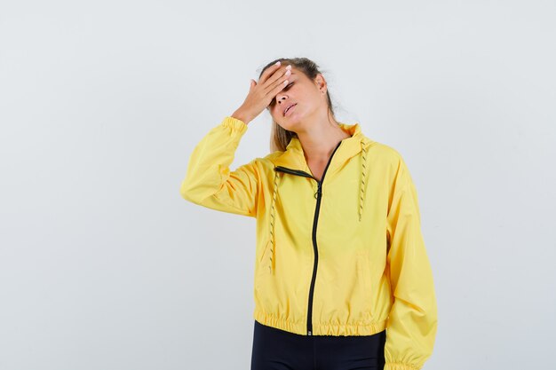 Blonde woman having headache in yellow bomber jacket and black pants and looking tired