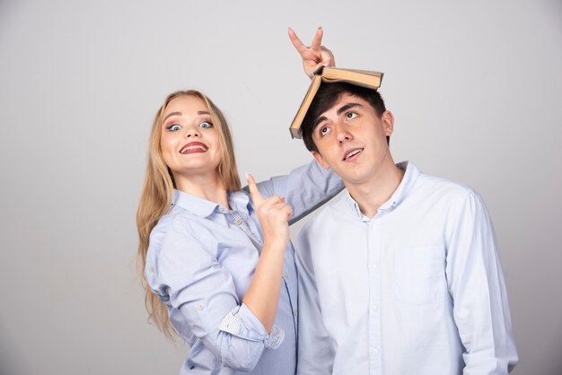 Blonde woman holding a book on head brunette man on gray wall