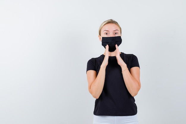 Free Photo blonde woman holding hands near mouth to tell secret in black t-shirt, white pants