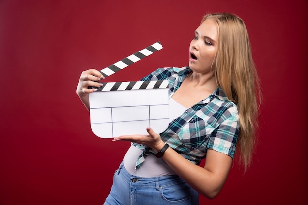 Free Photo blonde woman holding a movie production clapper board and looks confused and tired.