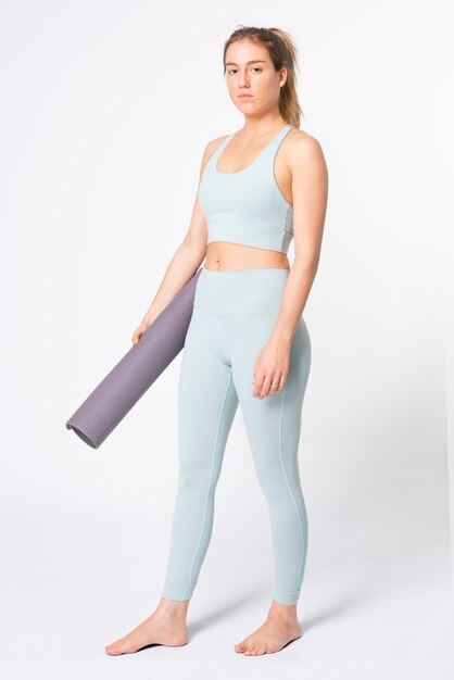 Blonde woman holding yoga mat in blue sports bra and leggings full body