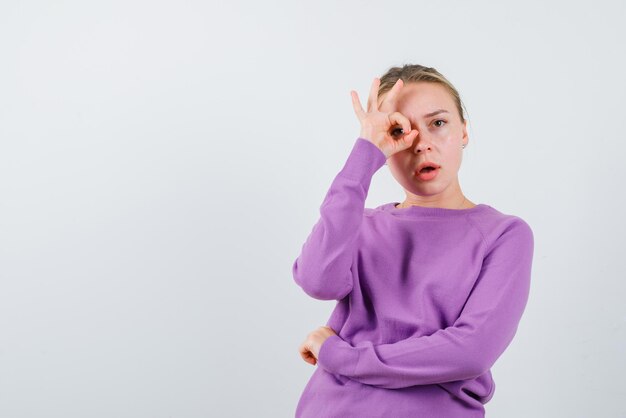 The blonde woman is holding her fingers around eyes on white background