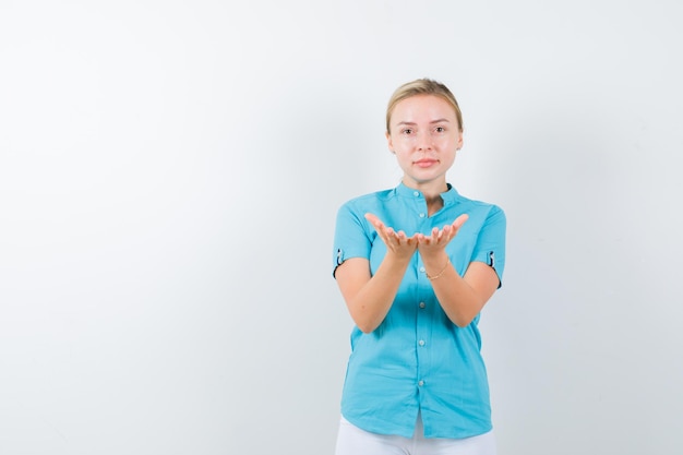 Blonde woman making giving or receiving gesture in blue blouse and looking gentle