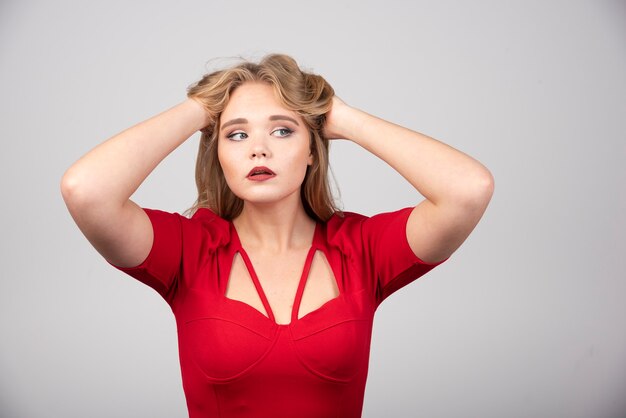 Blonde woman in red outfit holding her hair.