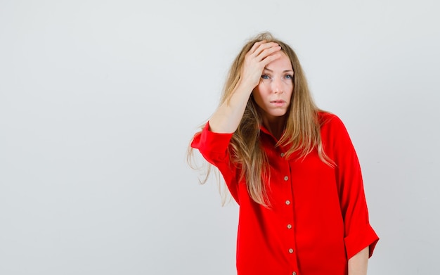 Blonde woman in red shirt holding hand on head and looking sorrowful ,